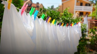 weiße Wäsche hängt mit bunten Wäscheklammern an einer Wäscheleine
