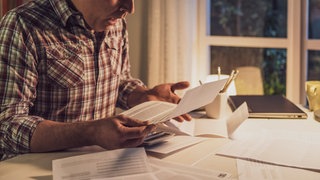 Ein Mann sitzt an einem Tisch und schaut etwas verzweifelt auf verschiedene Rechnungen.