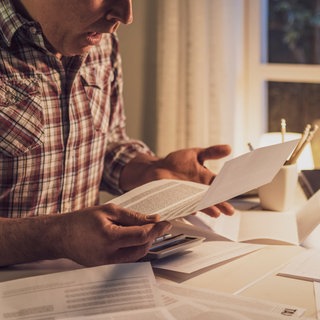 Ein Mann sitzt an einem Tisch und schaut etwas verzweifelt auf verschiedene Rechnungen.