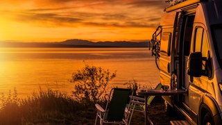 Wohnmobil und Campingstühle vor einem See