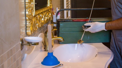 Mann reinigt Abfluss mit Rohrreinigungsspirale