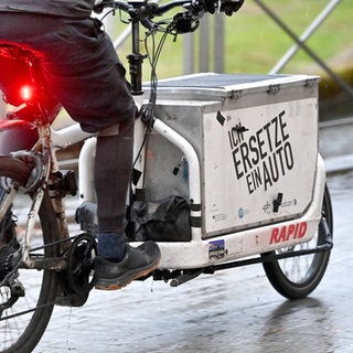 Lastenfahrrad: Jemand fährt mit einem Lastenfahrrad mit der Aufschrift "Ich ersetze ein Auto"