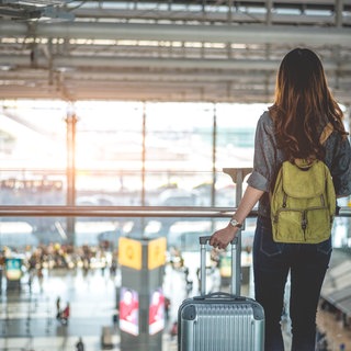 Frau steht auf einer Brücke und Blickt in die Flughafenhalle