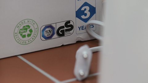 Mehrere Siegel, darunter das GS-Zeichen auf der Verpackung eines Elektrogeräts; ein Kabel unscharf im Vordergrund 
