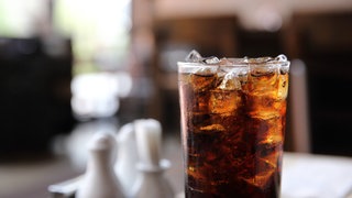 Ein Glas Cola mit Eiswürfeln steht auf einem Tisch
