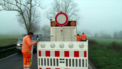 Ein Mitarbeiter der Straßenmeisterei stellt Schilder auf und sperrt eine Landstraße ab
