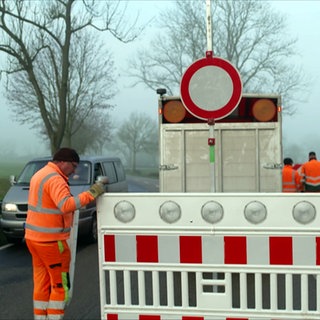 Ein Mitarbeiter der Straßenmeisterei stellt Schilder auf und sperrt eine Landstraße ab