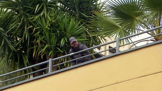 Ein Mann schaut über das Geländer eines Parkhaus-Decks in Stuttgart. Nebem ihm stehen Pflanzen.