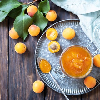 Aprikosenkonfitüre in einem Glas auf einem silbernem Tablett; Aprikosen liegen auf dem Tisch