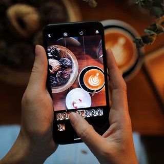 Jemand fotografiert mit dem Smartphone einen Capuccino