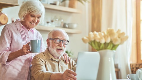 Älterer Mann am Laptop und ältere Frau mit Kaffeetasse