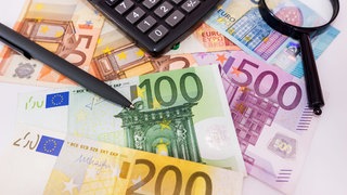 Geld, Taschenrechner und Lupe liegen auf dem Tisch