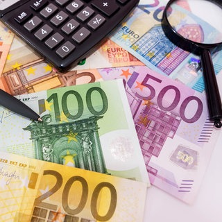 Geld, Taschenrechner und Lupe liegen auf dem Tisch