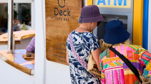 Zwei Touristinnen stehen im Urlaub an einem Bankautomaten.