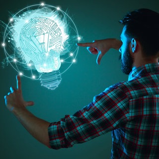 Ein Mann steht vor blauem Hintergrund und zeigt mit Fingern auf fliegende Glühbirnenzeichnung.