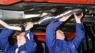 Automechaniker bauen im November 1987 in einer Autowerkstatt einen Abgas-Katalysator in einen Wagen ein.