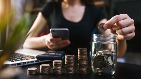 Frau wirft Geld in eine Glas und hält ein Handy in der Hand