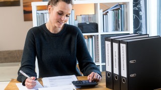 Eine junge Frau lächelt über ihre Steuererklärung | Warum ihr zum Jahresende schon an die Steuererklärung denken solltet