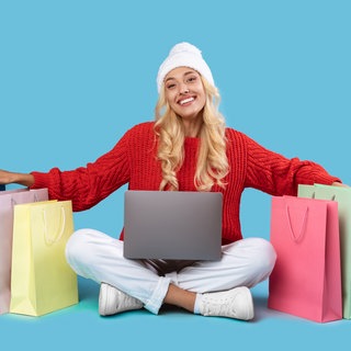 Frau sitzt am Laptop mit Tüten um sie rum