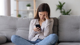Frau sitzt auf der Couch und schuat in ihr Smartphone