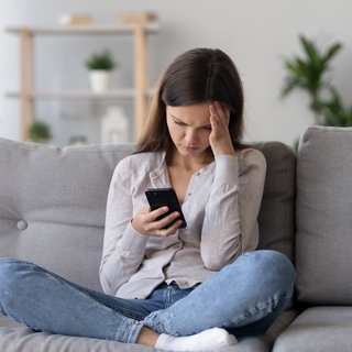 Frau sitzt auf der Couch und schuat in ihr Smartphone