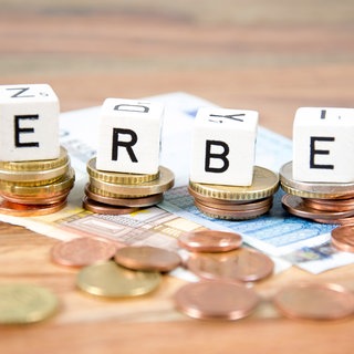 Mit Buchstaben-Würfeln wird das Wort "Erbe" gelegt. Die Würfel liegen auf Geldscheinen und Münzen.