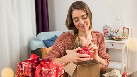 Eine junge Frau verpackt Weihnachtsgeschenke | Weihnachten 2025: Das sind die Versandfristen für Pakete und Briefe