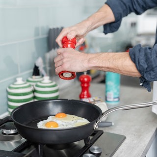 Mann würzt Spiegelei mit Gewürzmühle