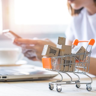 Shopping cart with Paper box or parcel with blur background woman holding mobile phone. Businesswoman or entrepreneur working from home. Online shopping, e-commerce,internet banking, spending money.