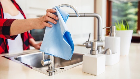 Spüle und Wasserhahn in der Küche werden mit einem Tuch gereinigt