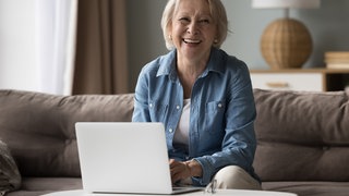 Eine Frau sitzt mit einem Notebook vor sich auf dem Sofa