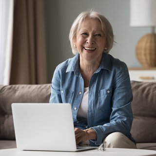 Eine Frau sitzt mit einem Notebook vor sich auf dem Sofa