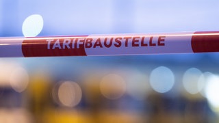 Ein Absperrband mit der Aufschrift "Tarifbaustelle". Gewerkschaften setzen sich für Arbeitnehmerrechte ein - und die auch oft mit Streiks durch. Streiks in Deutschland dauern oft Tage statt Stunden, immer weniger Beschäftigte sind Mitglied in Gewerkschaften.