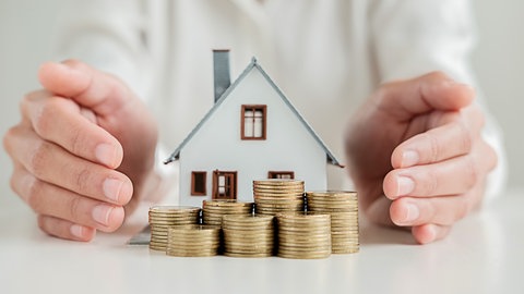 Geldanlage und Finanzen: Mehrere Stapel Münzen vor einem Modell-Haus