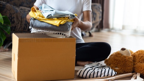 Eine Frau packt alte Kleidungsstücke in einen Karton