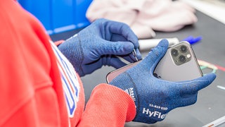 Ein Mitarbeiter von Rebuy hält ein gebrauchtes Smartphone in der Hand.Es gibt wenig günstige Smartphones. Dafür werden mehr generalüberholte Geräte gekauft. Was muss man bei refurbished Handys beachten? Wann lohnt sich rebuy oder second-hand?