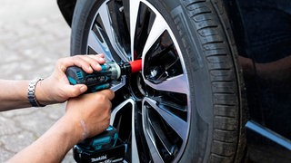 Ein Mann zieht die Radmuttern an einem Reifen nach | Radmuttern am Auto nachziehen – wer haftet, wenn sich ein Rad löst?