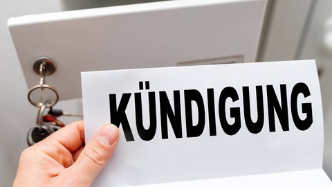 Eine Hand hält ein Kündigungsschreiben mit Aufschrift Kündigung vor einem geöffneten Briefkasten, symbolisch für den Verlust des Arbeitsplatzes.
