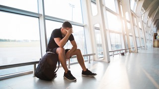 Ein trauriger junger Mann wartet am Flughafen auf seinen verspäteten Flug
