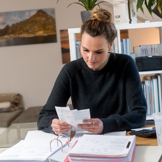 Eine Frau sitzt an ihrem Schreibtisch und macht die Steuererklärung | Wer nicht abgibt, verschenkt in der Regel ein paar hundert Euro: Warum ihr die Steuererklärung nicht aufschieben solltet