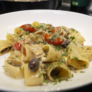 Nahaufnahme von Pasta Calamarata mit Thunfisch und Burrata. Serviert auf einem weißen Teller.