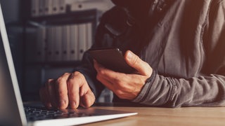 Hacker mit Handy und Laptop. Warum kann die Polizei bei georteten Handys häufig nicht helfen?