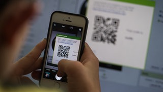 Eine Person hält ein Smartphone vor einen QR-Code und scannt diesen mit der Handykamera.