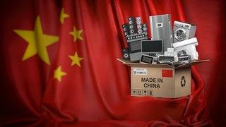 Hintergrund: Chinesische Flagge, Vordergrund: Kiste mit Elektrogeräten und Aufschrift "Made in China"