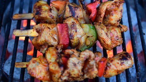 Fleischspieße liegen auf einem Holzkohle-Grill.