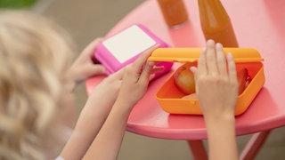 Kind öffnet seine Brotdose. Lunchboxen im Test, welche ist die beste? Wir vergleichen Tedi, Bio-Fabrik, Tchibo, Mepal, Koziol, Emsa, Ajaa, Ekobo, Bioloco von Chic Mic, Lekkabox.
