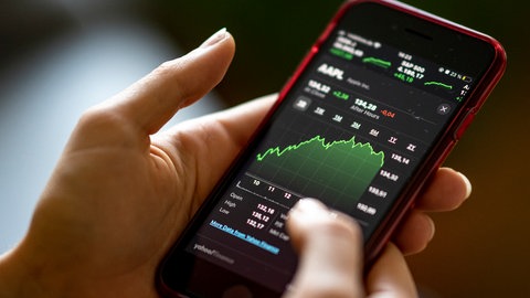 Eine junge Frau betrachtet auf ihrem Smartphone einen Aktienkurs.