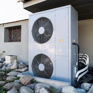 Die Lüftungsanlage einer Wärmepumpe steht vor einem Wohnhaus.
