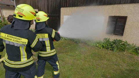 Feherwehrleute spritzen mit einem Feuerwehrschlauch auf eine weiß angestrichene Fläche. Wie gut ist die Fassadenfarbe vom Baumarkt Bauhaus?