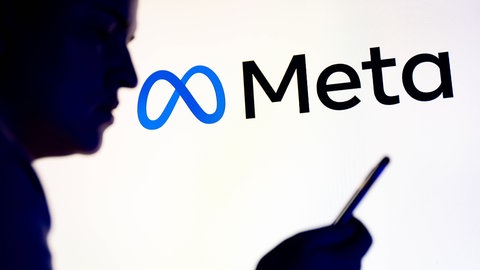 Mensch schaut auf Handy, im Hintergrund das Meta-Logo: Es gibt eine Sammelklage gegen Meta
